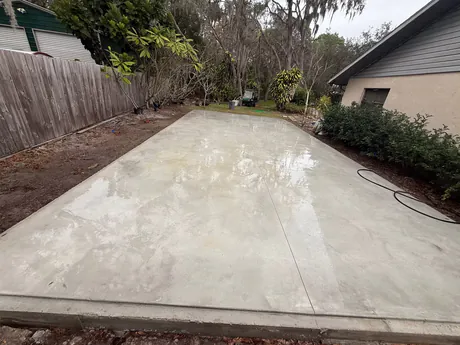 Freshly poured and floated concrete slab patio, still wet, formed square against a house wall.